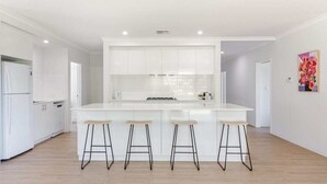 A modern kitchen with white cabinetry, a central island with stools, and a bright, neutral color palette. - Wildgreen Villa—Lakeside Hideaway in Winery Estate (Yallingup Siding)