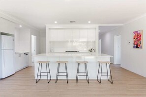 A modern kitchen with white cabinetry, a central island with stools, and a bright, neutral color palette. - Wildgreen Villa—Lakeside Hideaway in Winery Estate (Yallingup Siding)