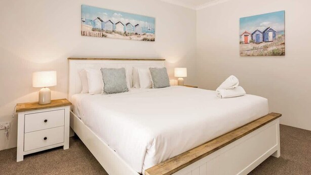 A bedroom with a bed, bedside tables, and two wall-mounted paintings. - Wildgreen Villa—Lakeside Hideaway in Winery Estate (Yallingup Siding)