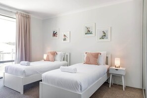 A hotel room with two single beds, a nightstand with a lamp, and framed bird artwork on the wall.