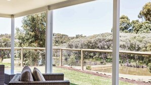 A covered outdoor seating area with wicker furniture, a view of a natural landscape with trees and a fenced pond. - Wildgreen Villa—Lakeside Hideaway in Winery Estate (Yallingup Siding)