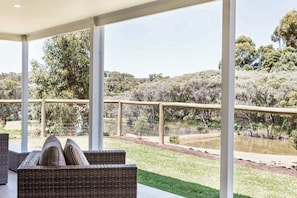 A covered outdoor seating area with wicker furniture, a view of a natural landscape with trees and a fenced pond. - Wildgreen Villa—Lakeside Hideaway in Winery Estate (Yallingup Siding)