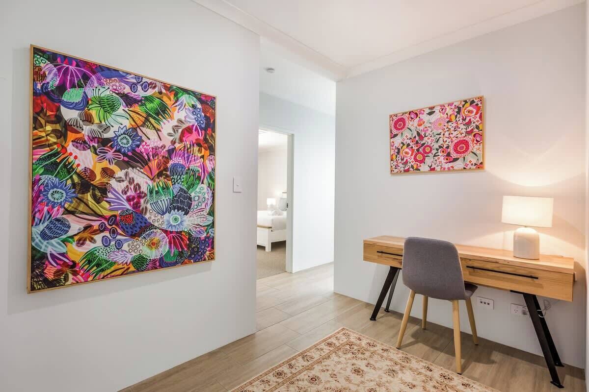 Ein Zimmer mit Schreibtisch, Stuhl und zwei Wandbildern.
