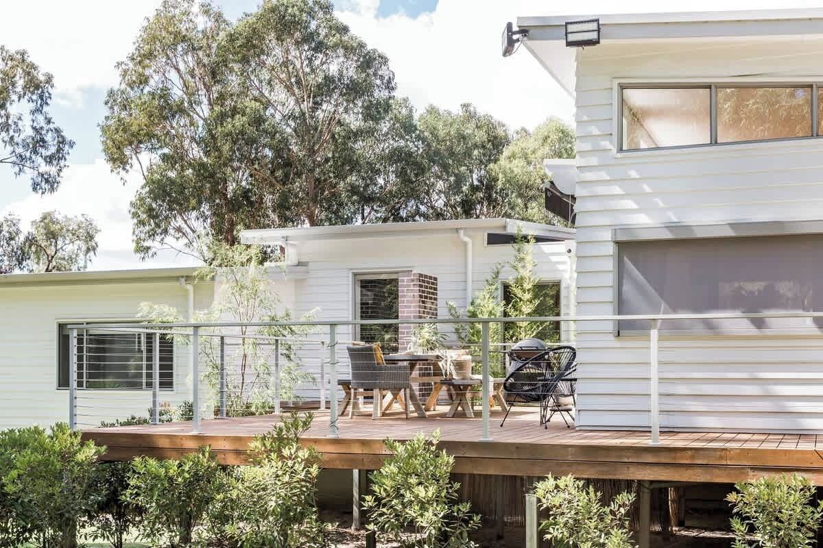 Una casa moderna con una terraza, mobiliario exterior y un ventanal grande.