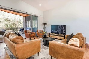 A modern living room with leather sofas, a coffee table, a TV, and a large window. - Twintrees—A Family Escape Surrounded by Nature (Dunsborough)