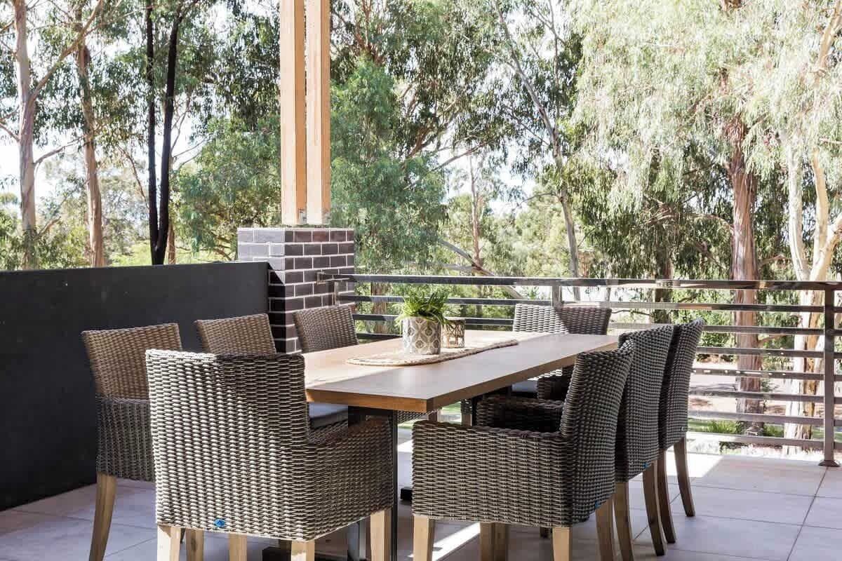 Un espacio de comedor al aire libre con mesa y sillas, rodeado por una barandilla y árboles.