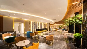 Een moderne lobby met een gebogen plafond, marmeren vloer en diverse zitplaatsen, waaronder banken en stoelen.