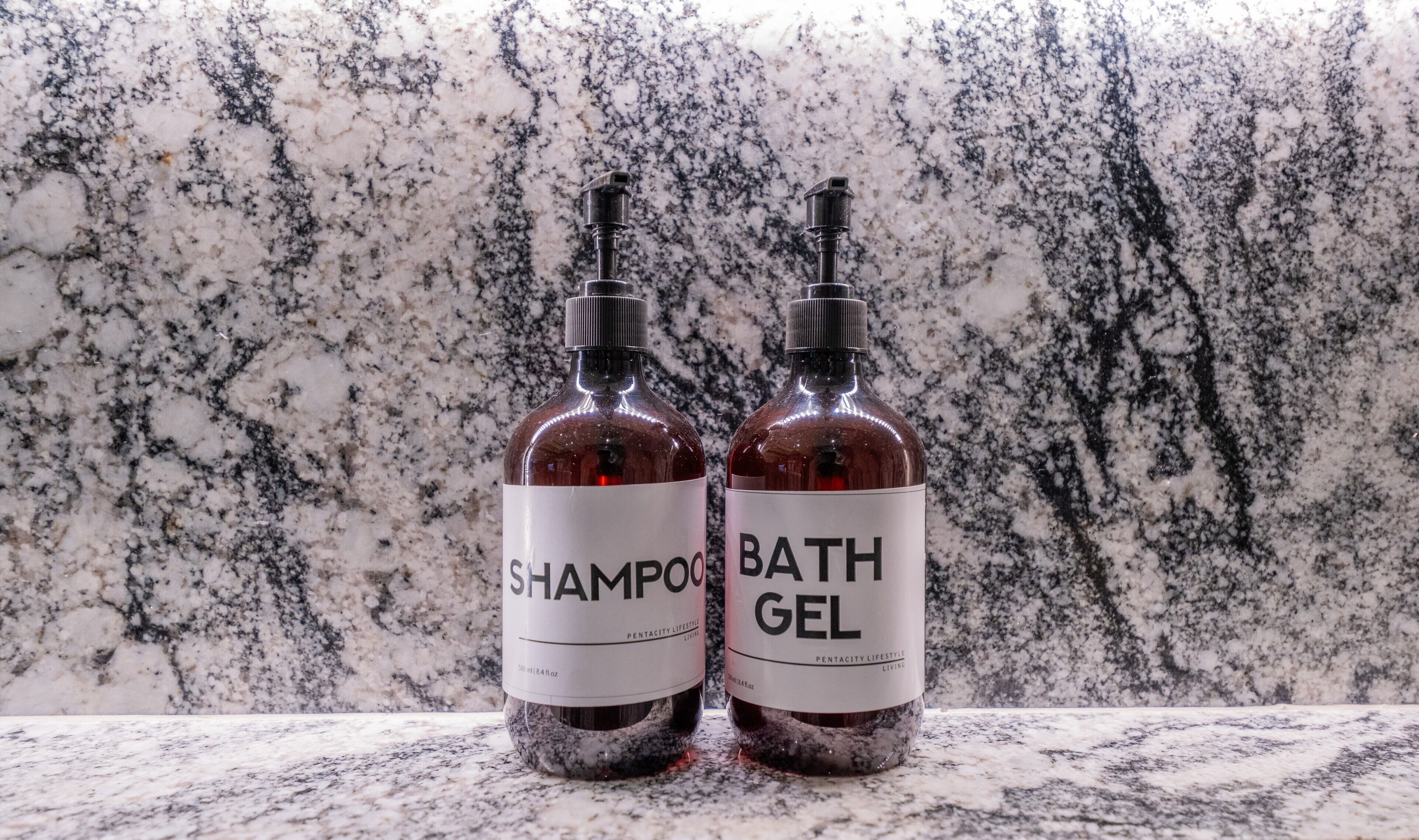 Zwei Flaschen Shampoo und Duschgel auf einer Marmorarbeitsplatte.