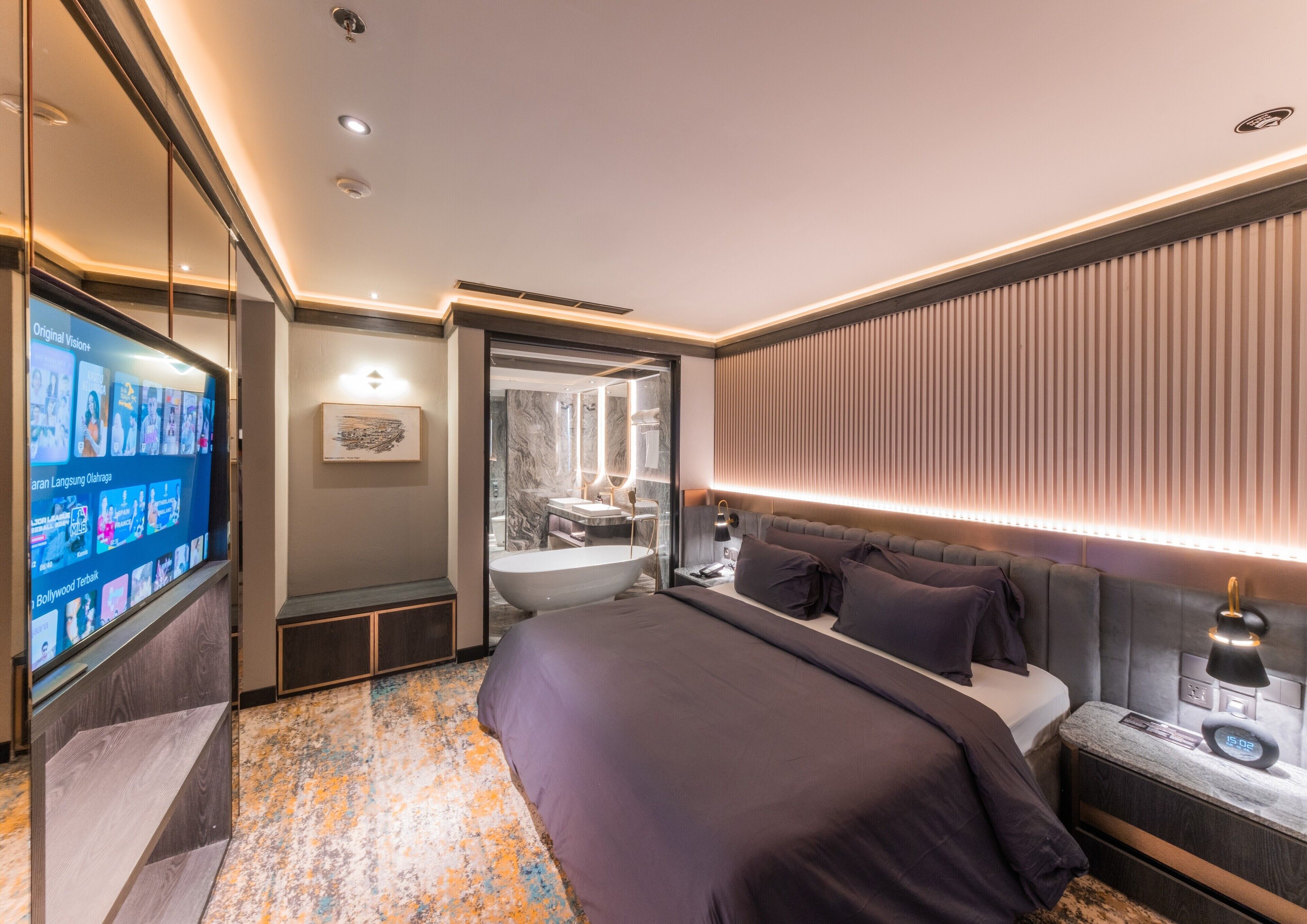 A modern hotel room with a large bed, a vanity with a mirror, a television displaying content, and a unique patterned carpet.