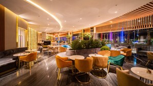 Een moderne lounge met ronde tafels en comfortabele zitmogelijkheden, met een weelderige plantencompositie in het midden en sfeerverlichting.