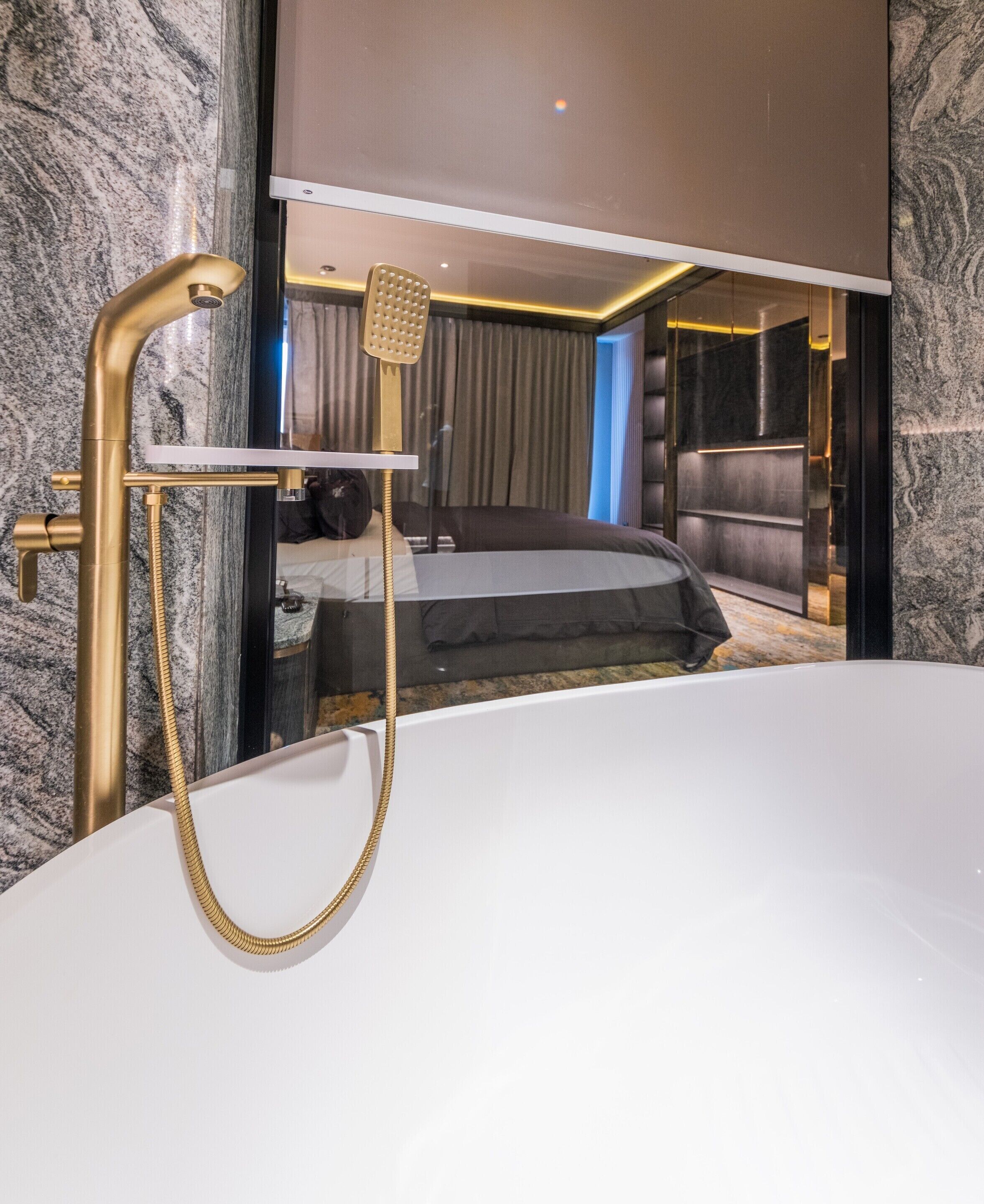 A modern bathroom with a gold showerhead, a white bathtub, and a marble wall.