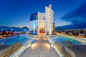 A modern hotel with a pool area, lounge chairs, and a view of the sea. - Pentacity Hotel Balikpapan (Balikpapan)