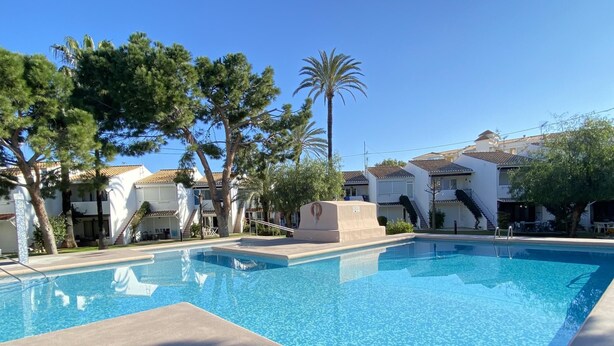 A swimming pool with a clear blue water, surrounded by trees and buildings with a tiled roof. - Bungalow 2 bedrooms for 5 people with swimming pool in Holiday Park urbanisation (Denia)