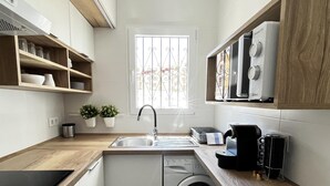 A compact kitchen with a washing machine, a coffee maker, and a window with a view of buildings. - Bungalow 2 bedrooms for 5 people with swimming pool in Holiday Park urbanisation (Denia)