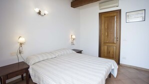 A bedroom with a bed, two wall-mounted lamps, a wooden door, and an air conditioning unit. - RESIDENZA LA SCOGLIERA - MONO N° 2 LA SCOGLIERA (Rio Marina)