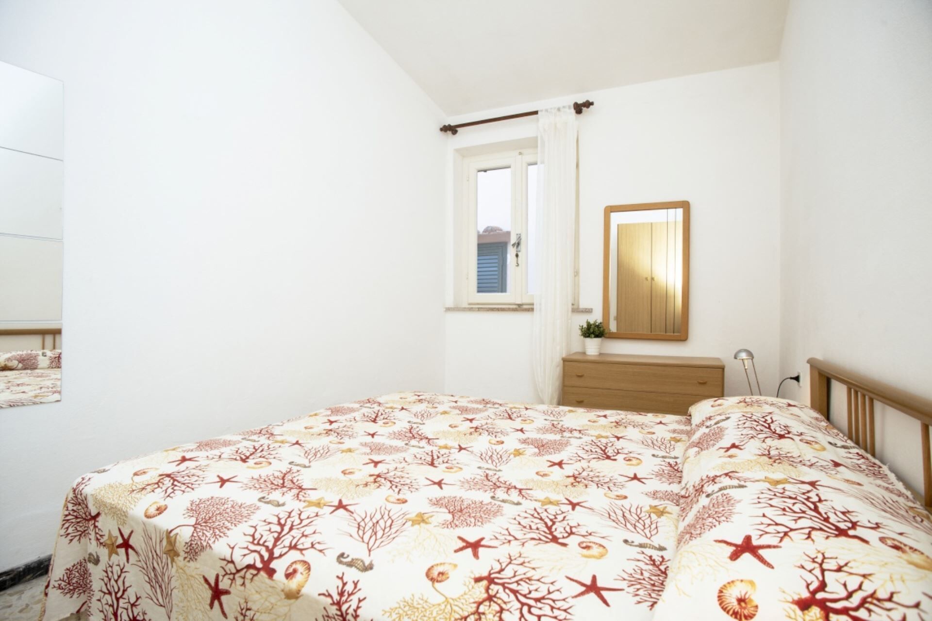 A bedroom with a bed, a dresser, a mirror, and a window with curtains.