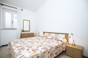 Un dormitorio con cama, mesita de noche, cómoda, espejo y ventana con cortinas.