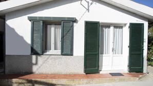 Un pequeño edificio con dos ventanas, cada una con contraventanas verdes, y una puerta blanca.