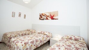 Una habitación con dos camas, techo blanco y una pared decorada con cuadros y una imagen grande de conchas marinas.