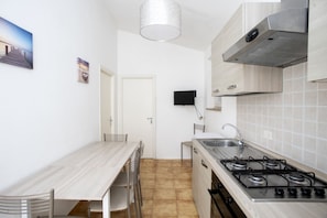Una cocina compacta con una mesa y sillas de madera, una estufa a gas, un lavamanos y un televisor de pared.
