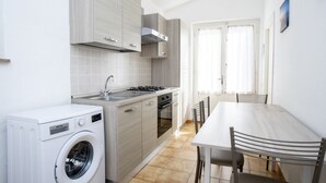 Cocina compacta con lavadora, estufa y zona de comedor con sillas.