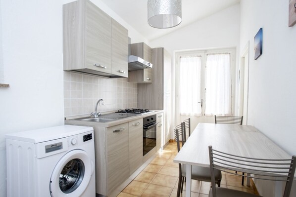 A compact kitchen with a washing machine, a stove, and a dining area with chairs.