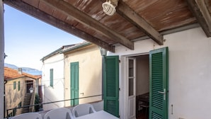 Un balcon avec une table et des chaises, des volets verts et une vue sur la mer.