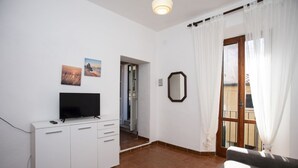 Une pièce avec un téléviseur posé sur un meuble blanc, un miroir au mur et une porte donnant sur un espace extérieur.