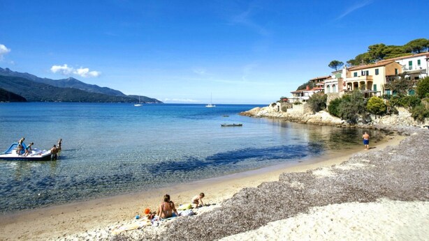 Une plage côtière aux eaux cristallines, bordée de bateaux et de bâtiments.