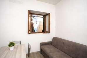 A small room with a wooden table, a brown sofa, and a window with an open shutter. - APP.TI SCAGLIERI - BILO SCAGLIERI (Portoferraio)