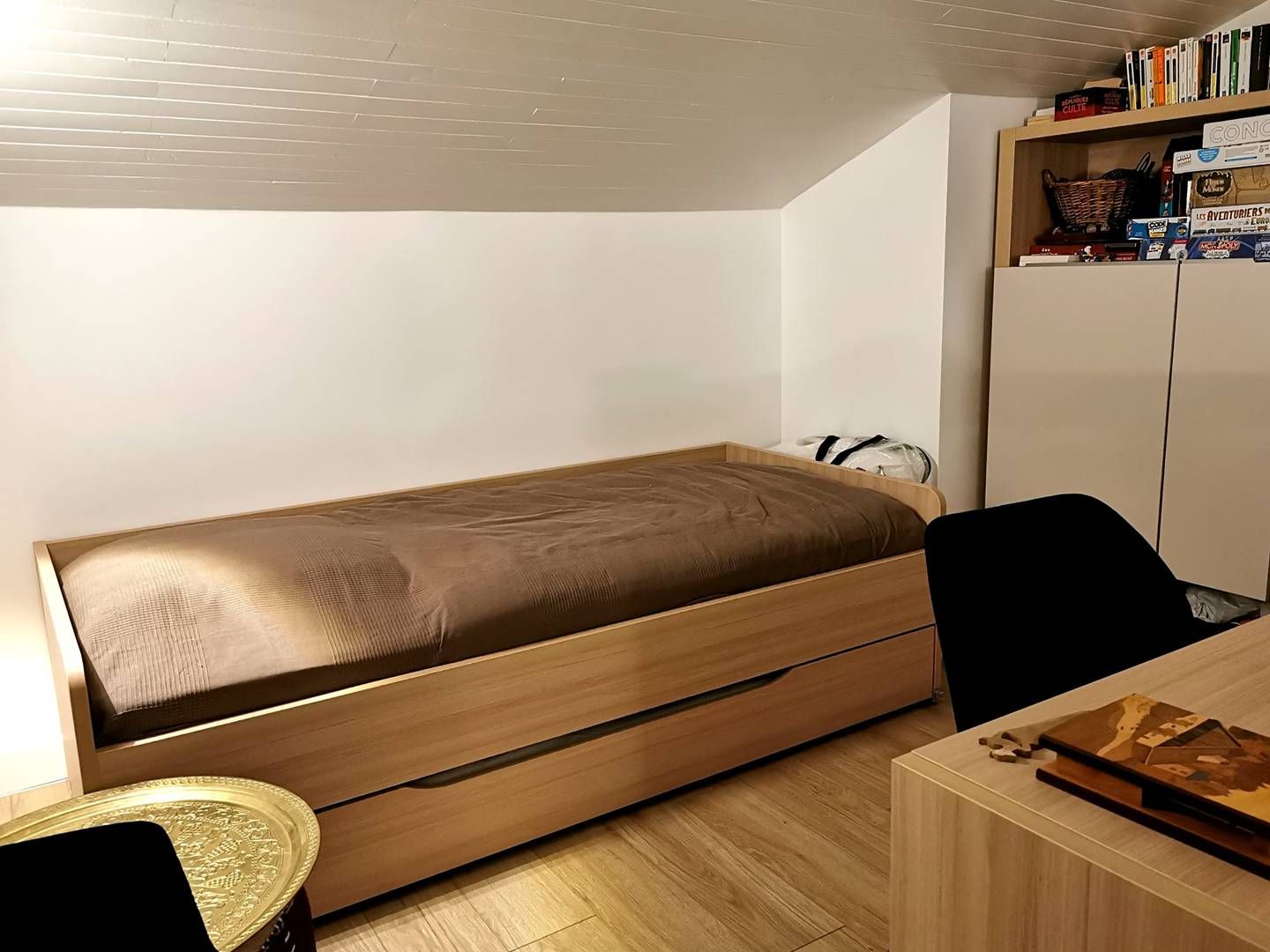 Una habitación pequeña con una cama individual, un escritorio y una estantería.