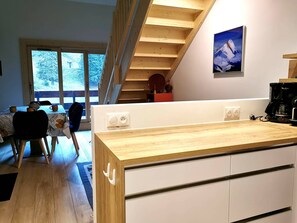 A modern kitchen with a wooden countertop, built-in cabinets, a coffee maker, and a view of a snowy landscape through a large window.