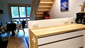 Una cucina moderna con piani in legno, mobili bianchi e piano cottura integrato. Si intravede sullo sfondo un'area pranzo con tavolo e sedie.