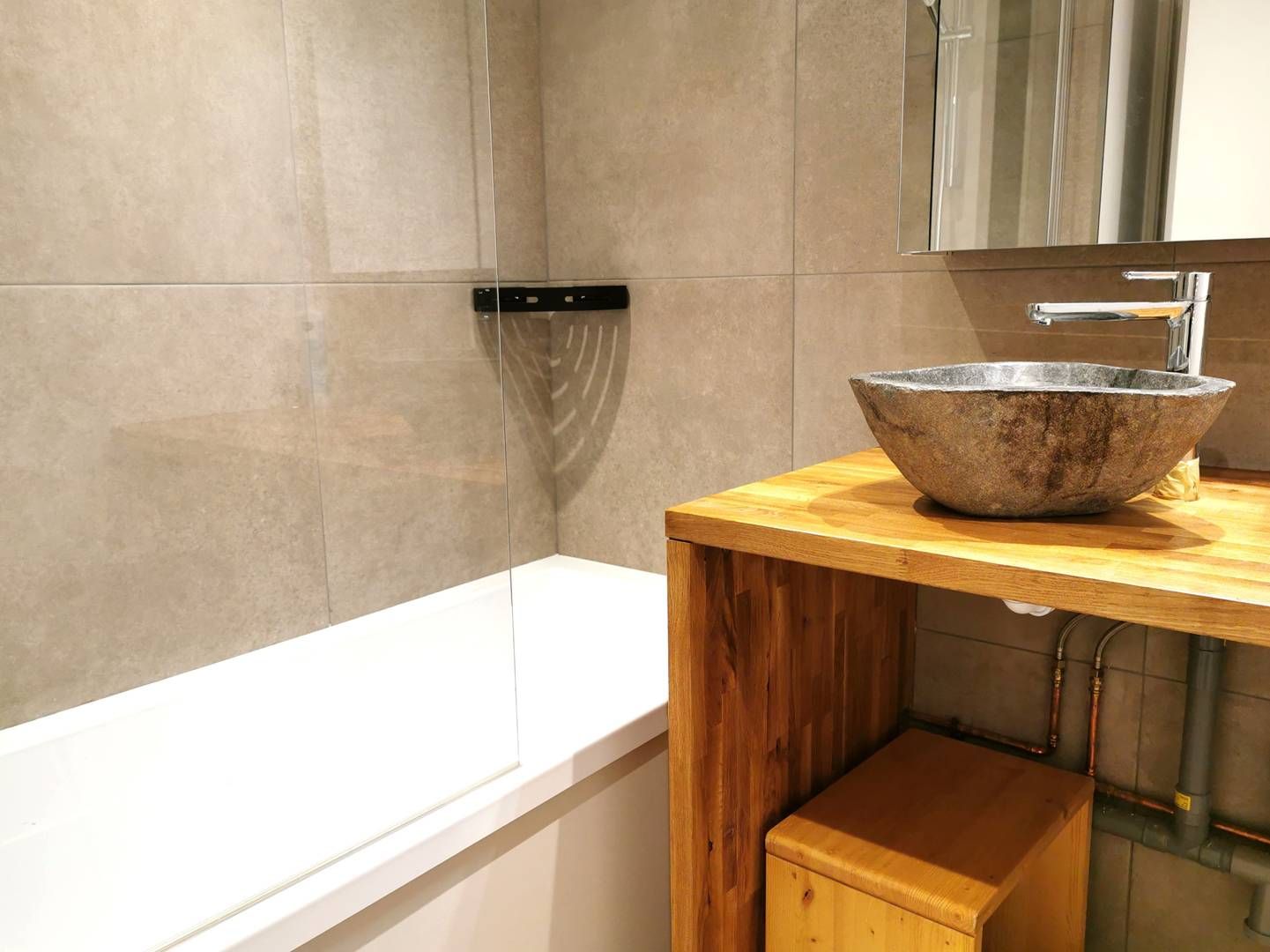 A bathroom with a white bathtub, a wooden vanity with a stone basin, and a mirror above the sink.