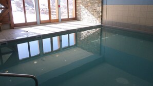 Una piscina interior con paredes de vidrio transparente, pared de piedra y suelo de baldosas.