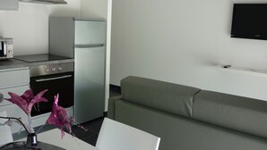 Eine moderne Küche mit Edelstahlkochfeld, Backofen und Kühlschrank. Im Wohnbereich befindet sich ein Flachbildfernseher an der Wand und ein grünes Sofa.