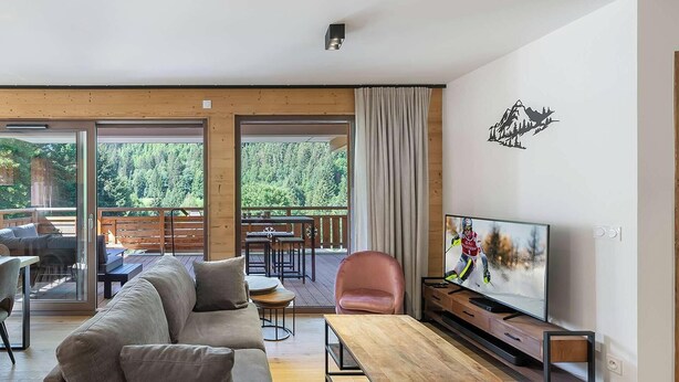 A modern living room with a sofa, a TV, a wooden table, and a balcony with outdoor furniture.