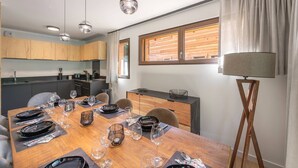 A modern dining area with a wooden table set for six, a kitchen in the background, and a floor lamp.