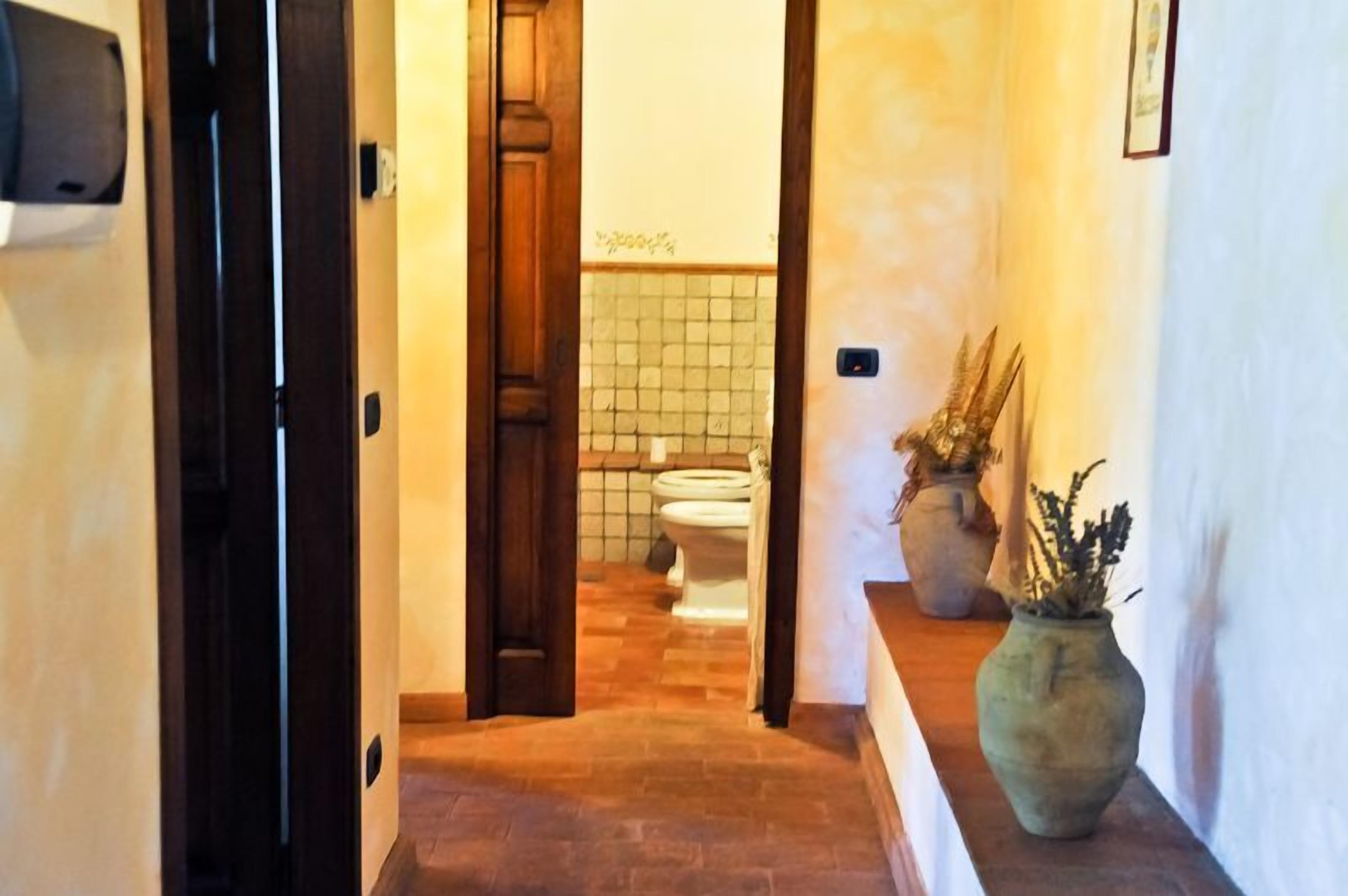 Un pasillo con puerta de madera, pared de azulejos, un inodoro y dos plantas en macetas.