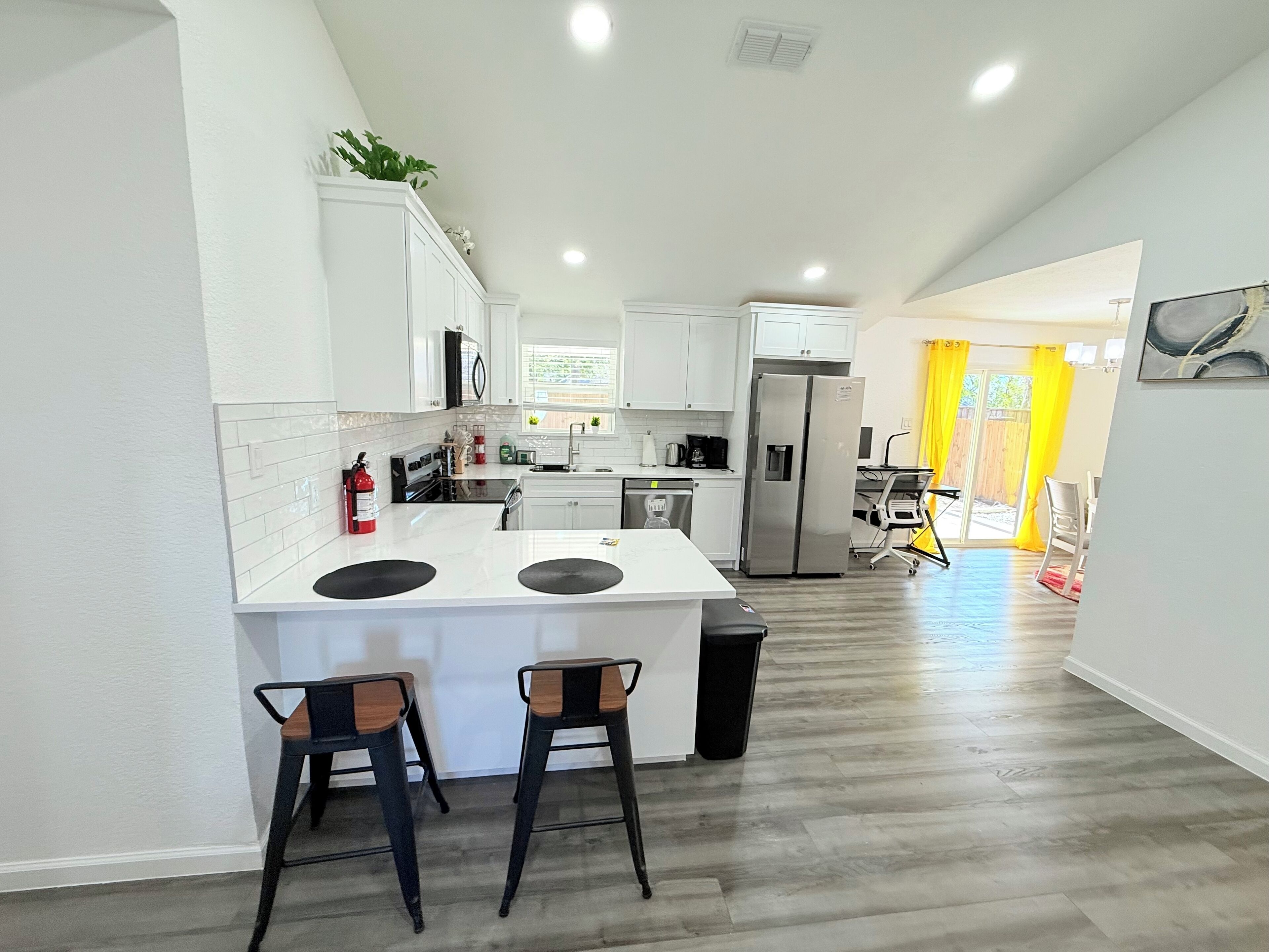 A modern kitchen with white cabinets, a stainless steel refrigerator, and a central island with stools.