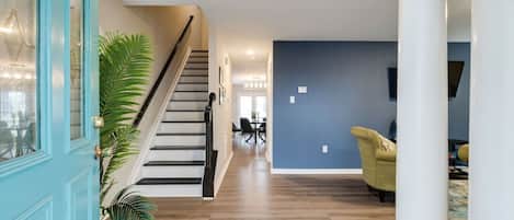 A spacious living area with a staircase, wooden flooring, and a blue accent wall.