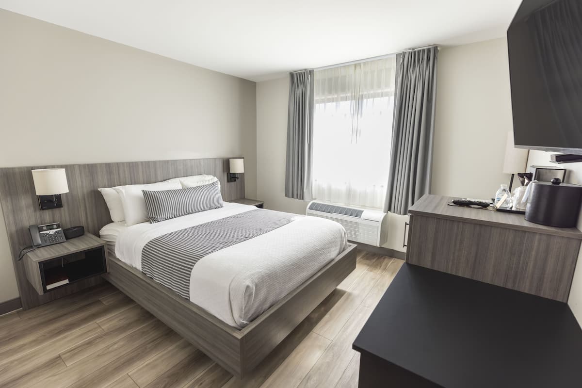 A modern hotel room with a wooden bed, bedside tables, a desk, and a large window with curtains.