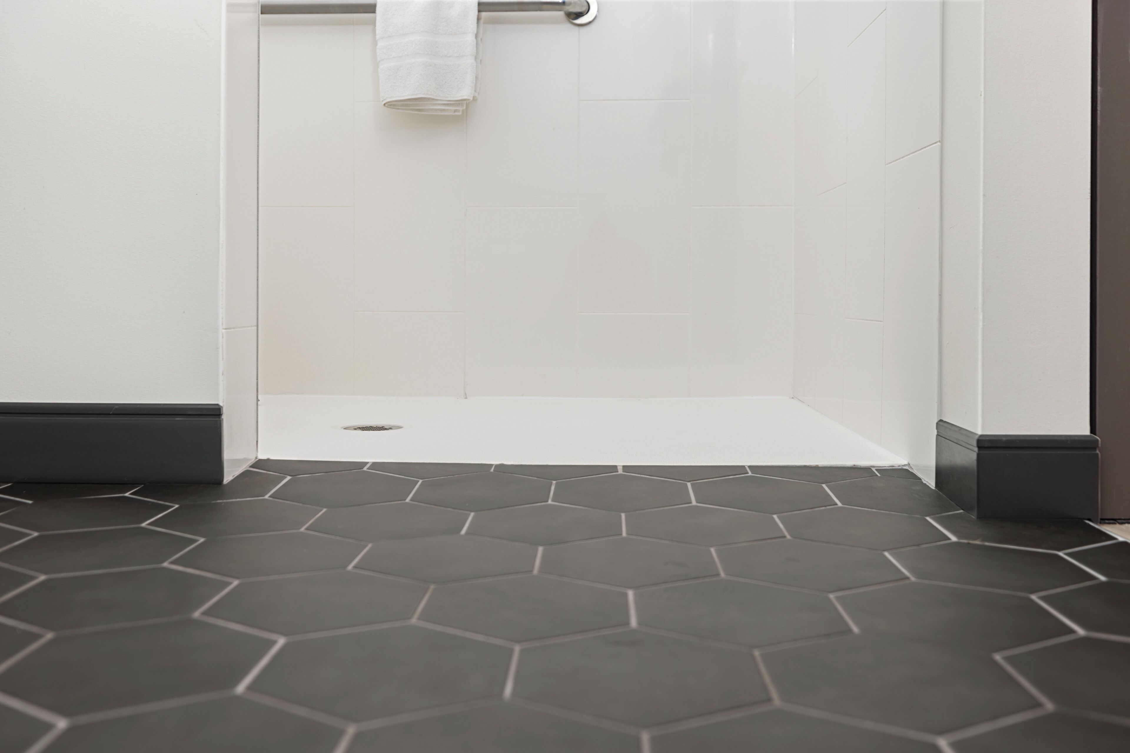 A bathroom with a shower area, white tiled walls, and a dark hexagonal floor pattern.