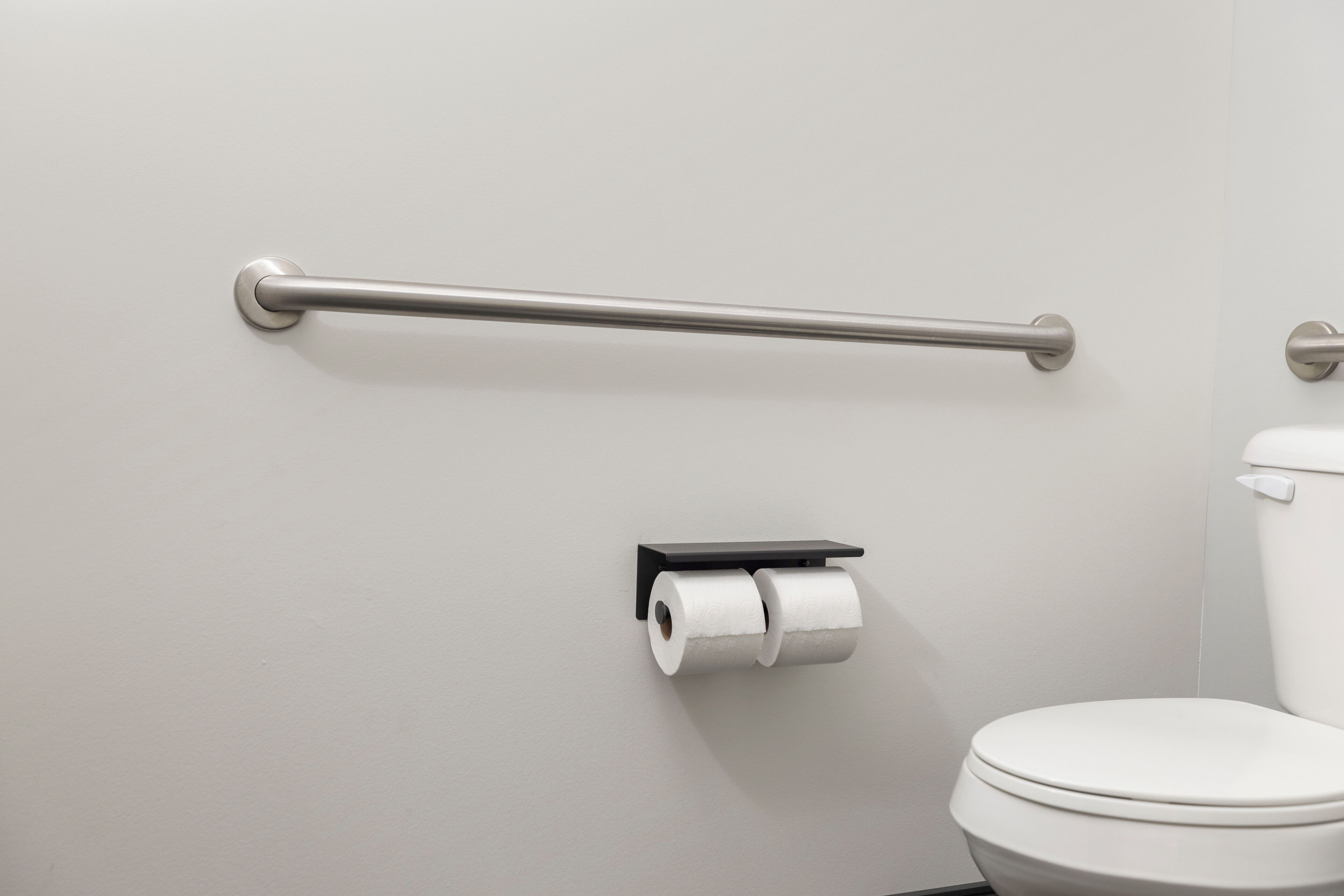 A bathroom with a toilet, a toilet paper holder, and a grab bar.