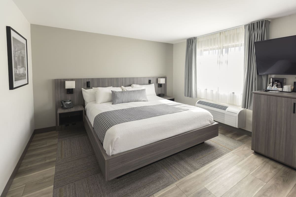 A modern hotel room with a large bed, bedside lamps, a flat-screen TV, and a built-in air conditioning unit.