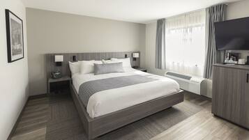A modern hotel room with a large bed, bedside lamps, a flat-screen TV, and a built-in air conditioning unit.