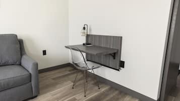 Une pièce moderne avec un canapé gris, un bureau avec une chaise et une étagère fixée au mur.