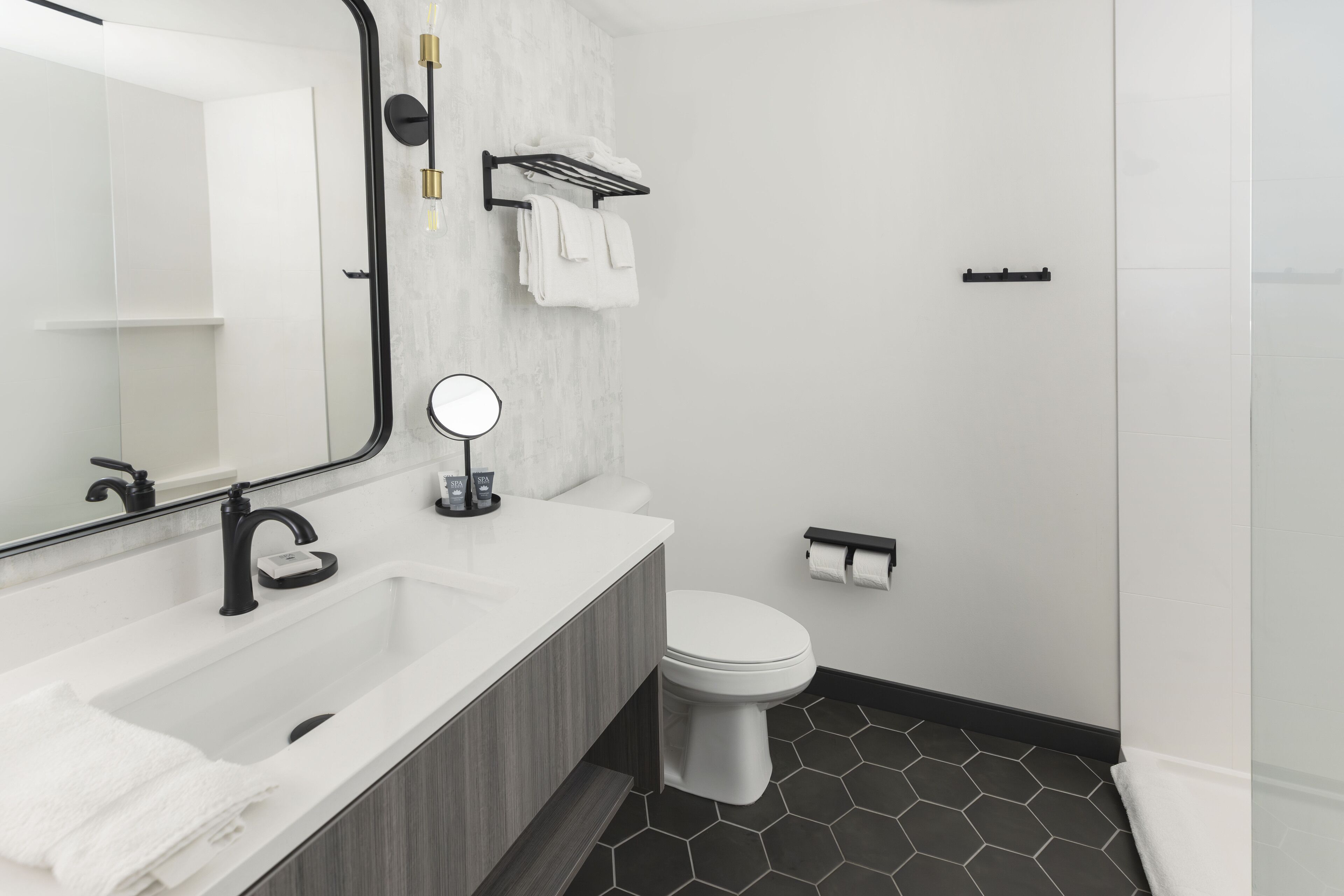 A modern bathroom with a white sink, black faucet, and a mirror with a round frame.