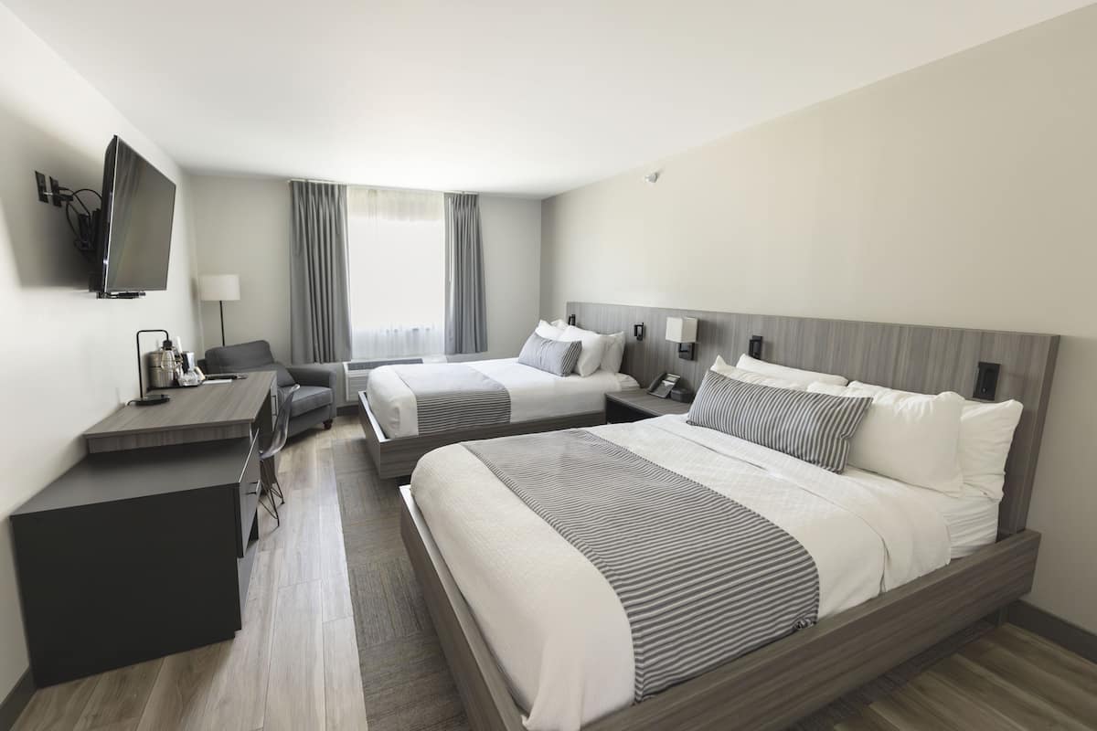 A hotel room with two beds, a desk, a TV, and a window with curtains.