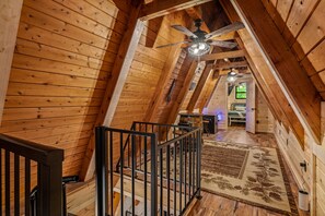 A wooden interior with a sloped ceiling, a ceiling fan, a staircase with a metal railing, and a patterned rug.